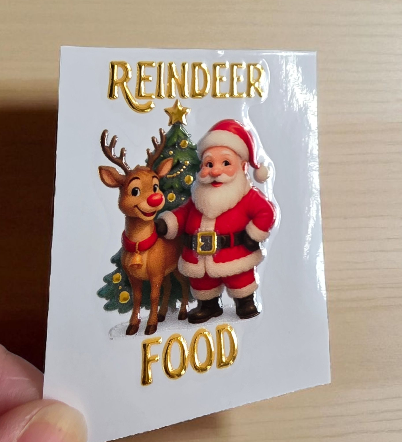 Sticker with Santa Claus and reindeer holding a Christmas tree, labeled 'Reindeer Food'.