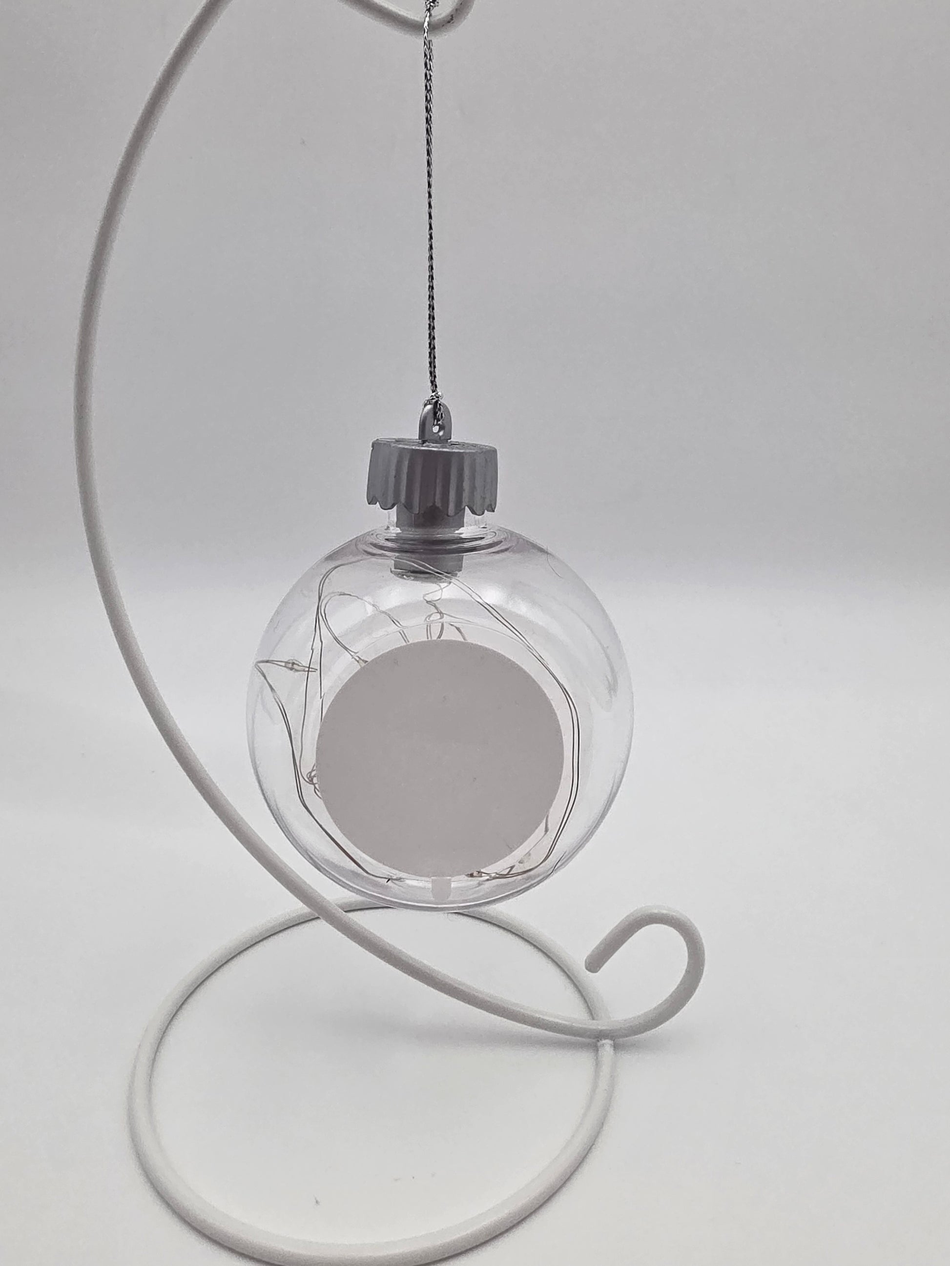 Clear glass ornament with wire design on a white stand against a light gray background