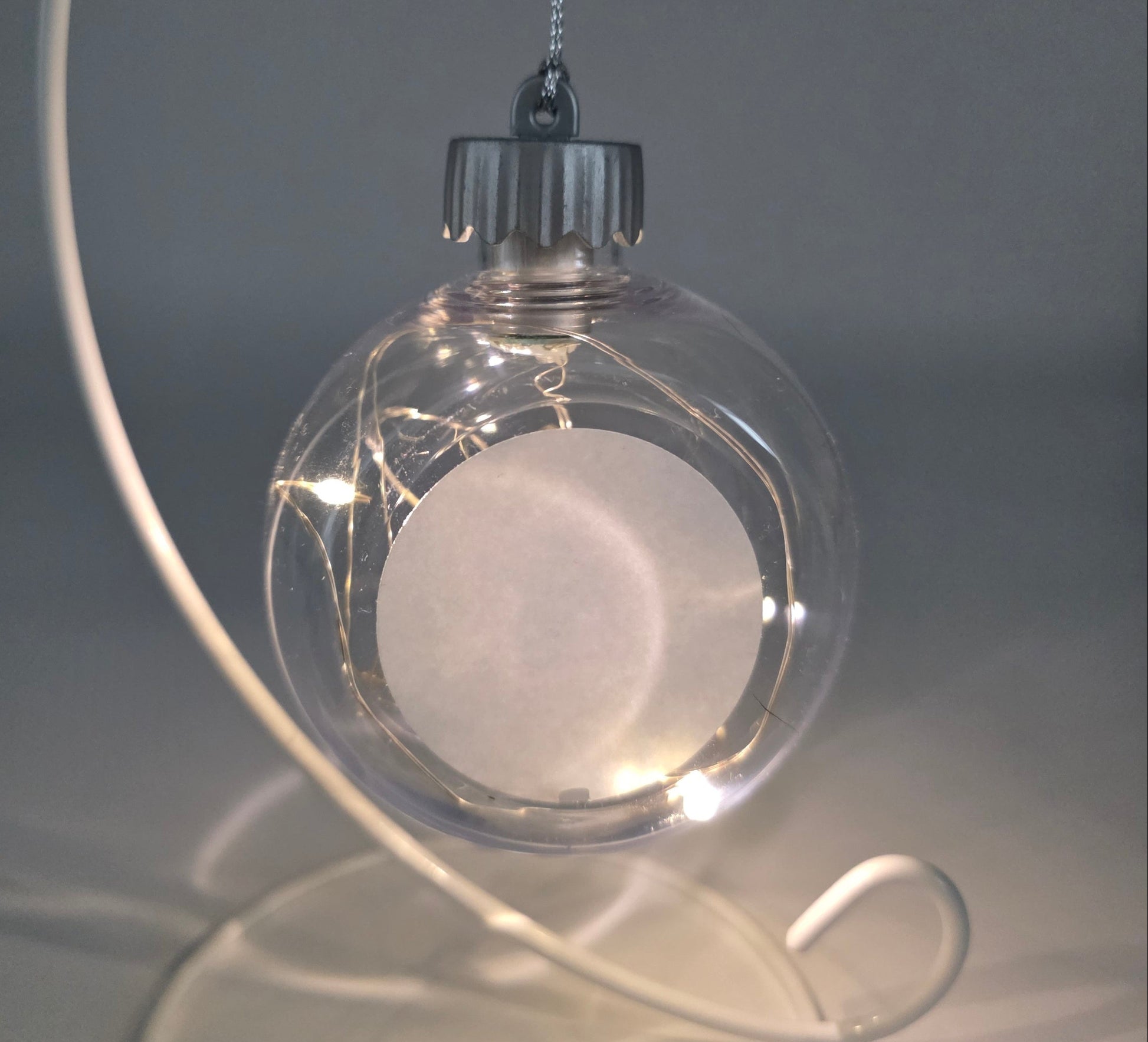 Clear glass ornament with a white sphere inside, hanging against a neutral background
